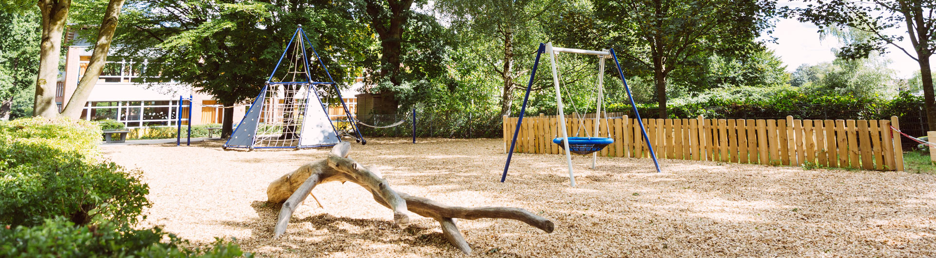 Das Bild zeigt einen leeren Spielplatz mit Schaukel und Klettergerüst.