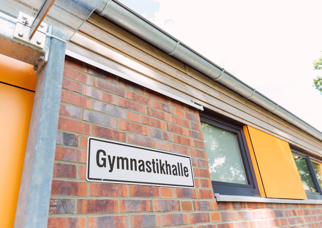 Das Bild zeigt einen Teil des neuen Schulgebäudes der Schule Lehmkuhle. An der Wand ist ein Schild mit der Aufschrift "Gymnastikhalle" angebracht. Dort befindet sich die neue Turnhalle.