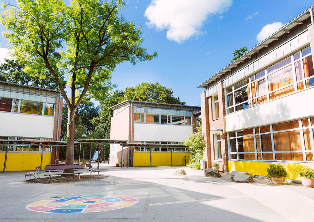 Das Bild zeigt den Schulhof der Schule Lehmkuhle. Auf dem Steinboden ist eine bunte Schnecke mit Zahlen aufgemalt zum Hüpfen.