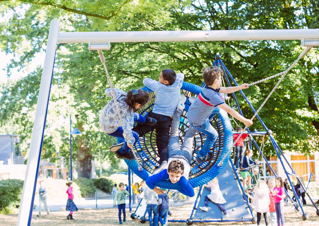 Das Bild zeigt eine große Nestschaukel in der sich vier Kinder befinden, die sehr hoch schaukeln und viel Spaß dabei haben.