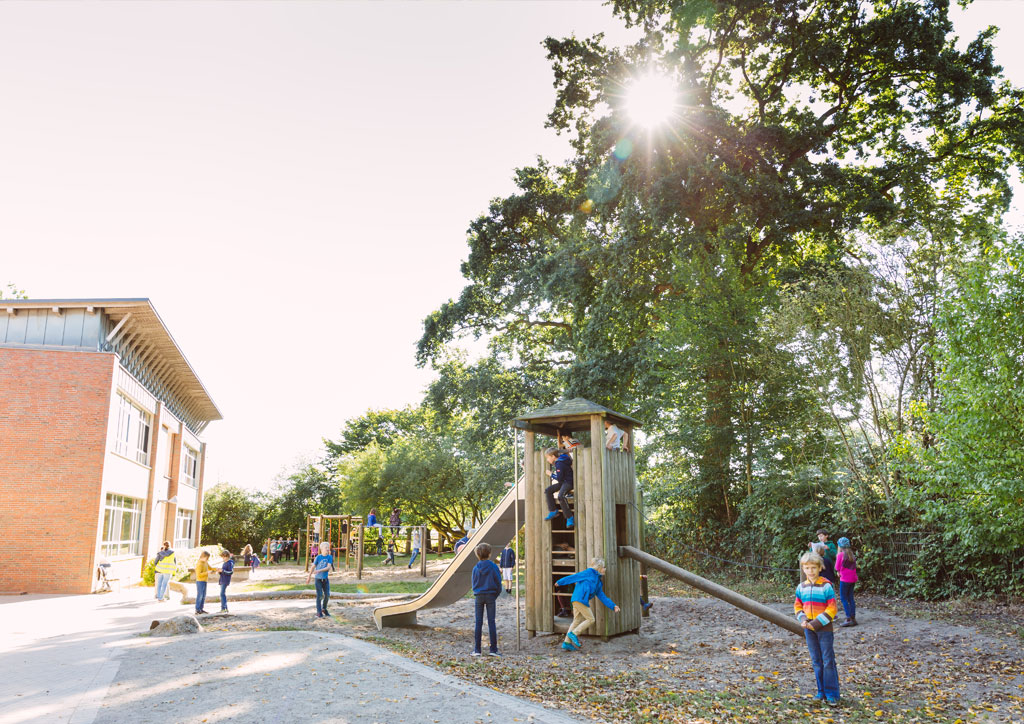 Das Bild zeigt den Holz-Rutschturm der Schule Lehmkuhle. Viele Kinder spielen dort. Dahinter befinden sich noch Kletterstangen.