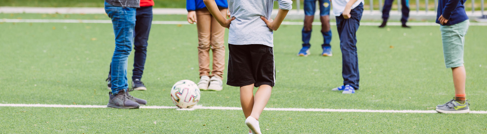 Viele Schüler stehen auf einem Fußballfeld. Man sieht nur die Beine und Füße.