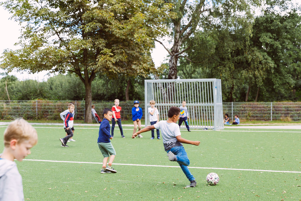 Das Bild zeigt einen Teil des Fußballplatzes der Schule Lehmkuhle. Dort spielen einige Jungs Fußball.