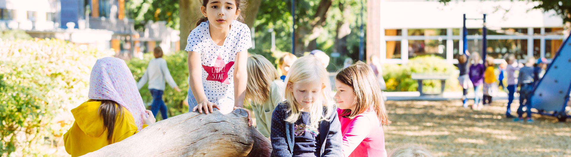 Einige Schüler spielen auf dem Schulhof und klettern auf einem Baumstamm.